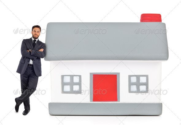 Businessman leaning against a miniature house